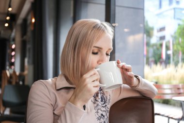 blond woman drinking coffee or tea in a cafe in the morning