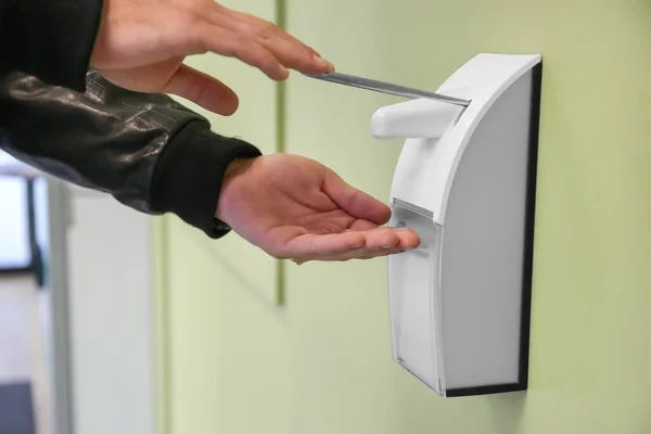 male hand with antibacterial gel from automatic sanitize machine hanging on building wall healthcare concept outdoor