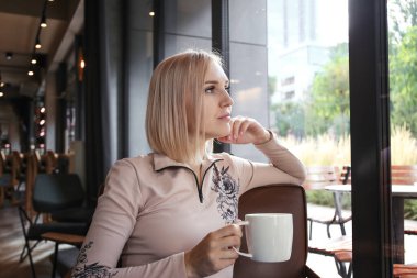 blond woman drinking coffee or tea in a cafe in the morning