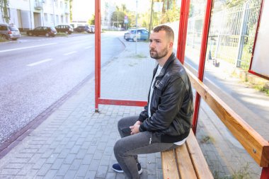 Bir adam otobüs durağında oturur otobüs, tramvay, tramvay otobüsü bekler. İşe, okula, üniversiteye toplu taşıma araçlarıyla gitmek. Geç kaldın. Yönlendirme zamanlaması.