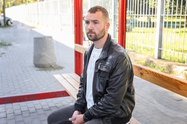 Bir adam otobüs durağında oturur otobüs, tramvay, tramvay otobüsü bekler. İşe, okula, üniversiteye toplu taşıma araçlarıyla gitmek. Geç kaldın. Yönlendirme zamanlaması.