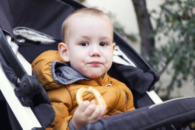 child eats a bun while sitting in a stroller