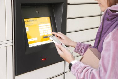 Warszaw, Polonya - Ağustos 2022: Elinde akıllı telefon ve posta terminalinin yanındaki paket olan kadın. Paket teslim makinesi.