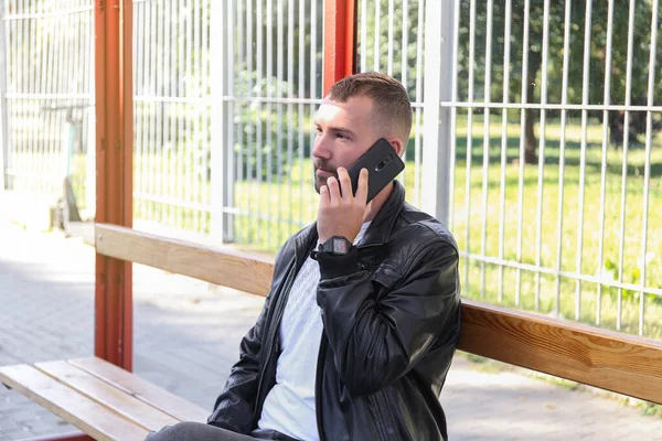 a man holding phone at a bus stop waiting for a bus, tram, trolley bus. Riding on public transport to work, study, university. Late. Route schedule.