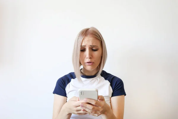 Emotional European Blonde woman frustrated looks at the phone