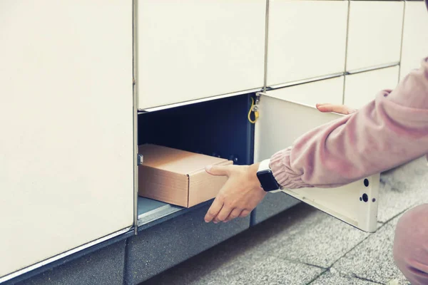 Woman takes the parcel in the self-service mail terminal. Parcel delivery machine.