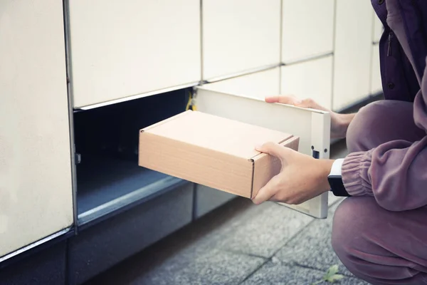 Woman takes the parcel in the self-service mail terminal. Parcel delivery machine.