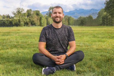 Mutlu adam çimenlerin üzerinde oturuyor doğanın ve dağların arkasında. Tatil