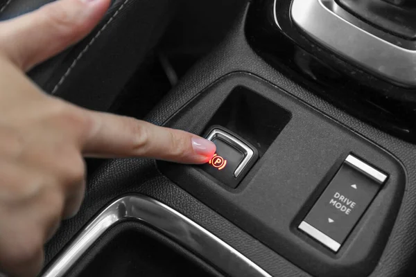Kadın arabadaki elektronik el frenine basıyor.