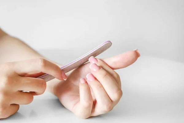 A girl with beautiful long nails makes a manicure with a nail file on a white background, close up of hands