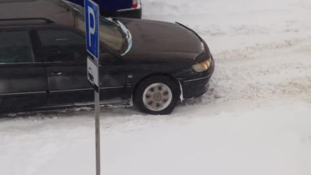 Ένα επιβατικό αυτοκίνητο γλιστράει στο χιόνι το χειμώνα και προσπαθεί να φύγει. Τροχός ολίσθηση στον πάγο σε χειμερινά ελαστικά. Μπλίζαρντ, κοντινό πλάνο — Αρχείο Βίντεο