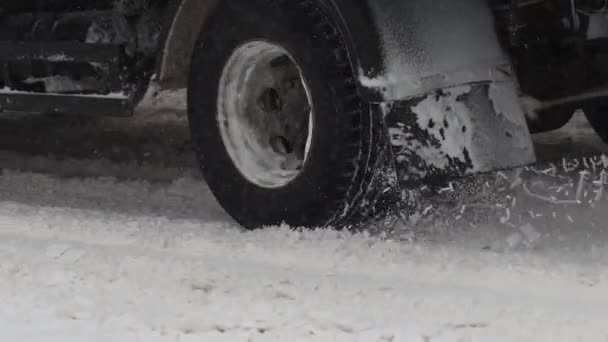 Nákladní auto jede v zimě po zasněžené silnici. Uzavření kola pneumatiky ve zpomaleném filmu. Špatné povětrnostní podmínky pro provoz, blizarde. Nebezpečí pro cestu — Stock video