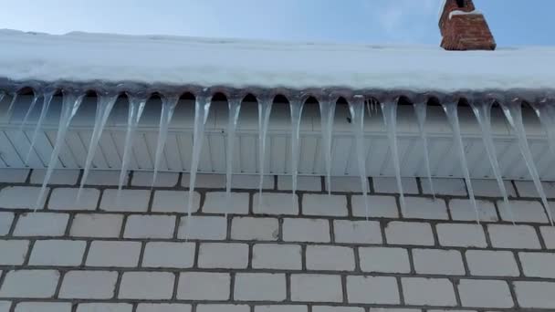 Eiszapfen hängen im Winter vor blauem, frostigen Himmel vom Schieferdach — Stockvideo