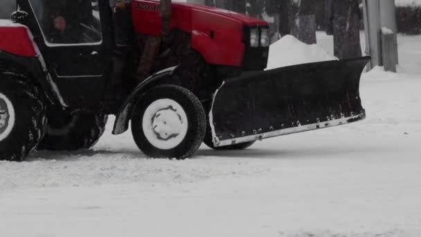 De winter. Tractor veegauto verwijdert sneeuw van de weg in de stad. Sneeuwval in slow motion. Gemeentelijke machines auto oogst reinigt de stad van sneeuw. Slechte weersomstandigheden voor het verkeer, sneeuwstorm — Stockvideo