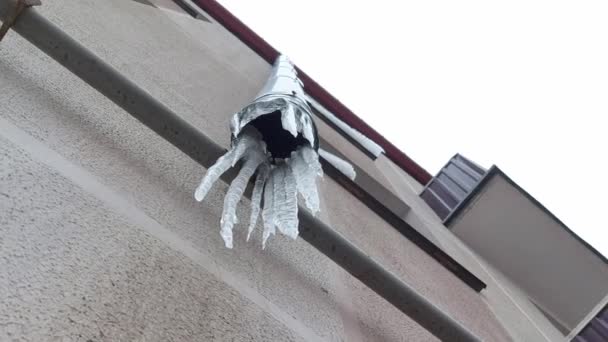 Frozen icicles hang in winter on a drainpipe on the wall of the house, outdoors — Stock Video
