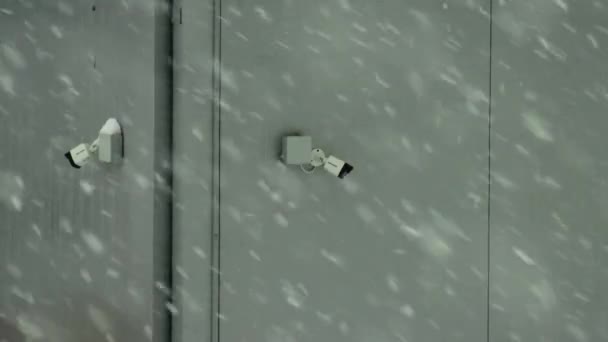 Две современные камеры видеонаблюдения на серой стене в снегопад зимой. Копия sapce для текста, безопасности — стоковое видео