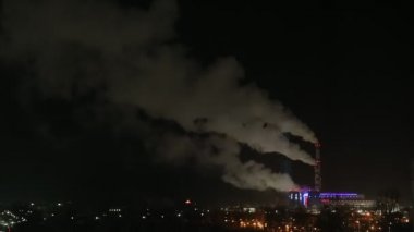 Soğuk bir kış gecesinde termik santralin bacalarından duman çıkıyor. Şenlikli şehir ışıkları, zaman atlaması