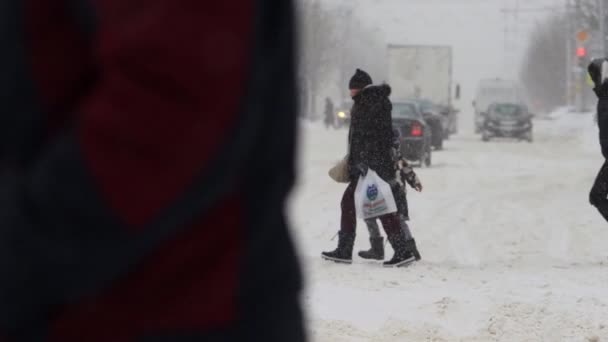 La gente camina en un cruce peatonal durante las nevadas en invierno. Los copos de nieve están cayendo en cámara lenta. Tormenta. Riesgo de lesión. Malas condiciones climáticas, ventisca. Navidad y Año Nuevo — Vídeos de Stock