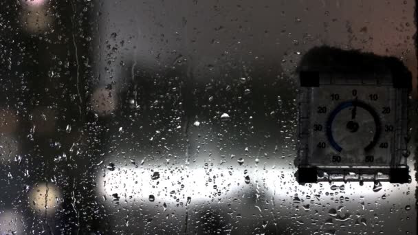 Vista desde la ventana a la calle durante el deshielo en invierno. La nieve mojada fluye por la ventana, un termómetro de calle con una gorra de nieve mojada. Copiar espacio para texto — Vídeos de Stock