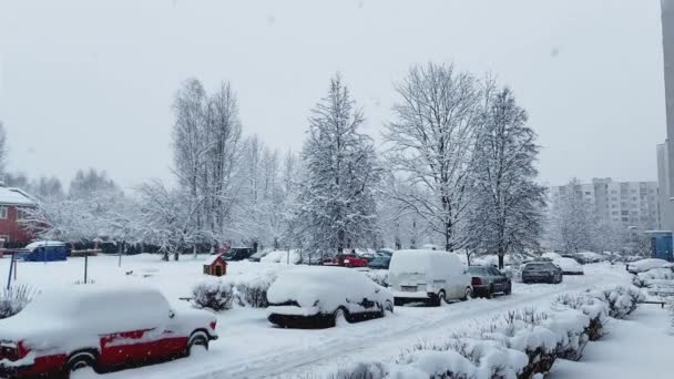 Припаркованные машины во дворе многоэтажного здания в зимнюю погоду в снегопад. Скользкая дорога, фон — стоковое видео