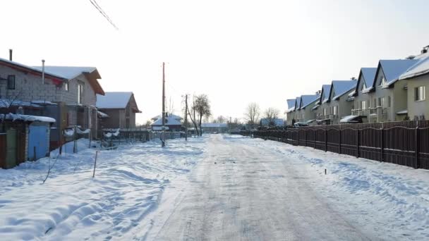 Domy wiejskie, droga wzdłuż ulicy w miejscowości w zimie. Mroźny dzień na tle słońca — Wideo stockowe