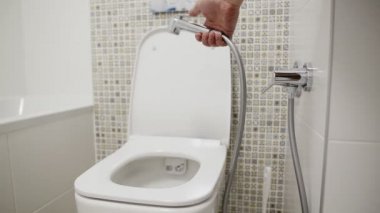 Dış cinsel organları yıkamak için hijyenik duşlu bir tuvalet. Hijyenik duş tutan bir el, yakın plan.