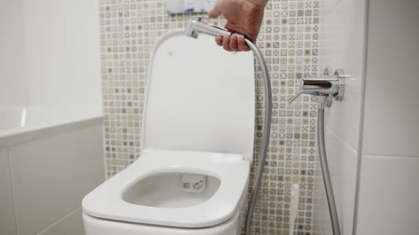 WC higiénikus zuhanyzóval a külső nemi szervek mosásához. Egy kéz, ami higiénikus zuhanyt tart, közelkép. — Stock videók