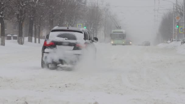 De winter. Auto 's rijden op een besneeuwde weg in de stad. Sneeuwval in slow motion. Slechte weersomstandigheden voor het verkeer, sneeuwstorm. Gevaar voor verkeersongevallen. Kruispunt — Stockvideo