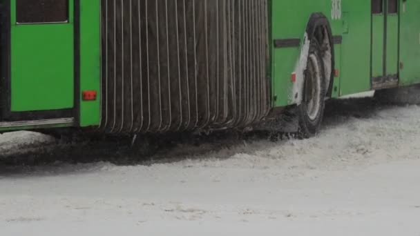 Kış. Şehir içi ulaşım otobüsü şehirde karlı bir yolda ilerliyor. Tekerlek lastiklerini yavaş çekimde kapatın. Kar yağışı. Trafik ve kar fırtınası için kötü hava koşulları. Trafik kazası tehlikesi — Stok video