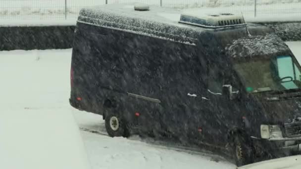 Снегопад в городе на фоне черного микроавтобуса зимой — стоковое видео