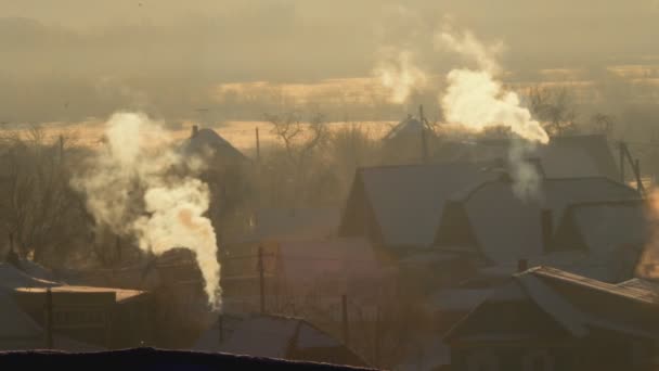 El humo naranja sale de las chimeneas del pueblo en una mañana helada de invierno. Amanecer en el pueblo, fondo — Vídeo de stock
