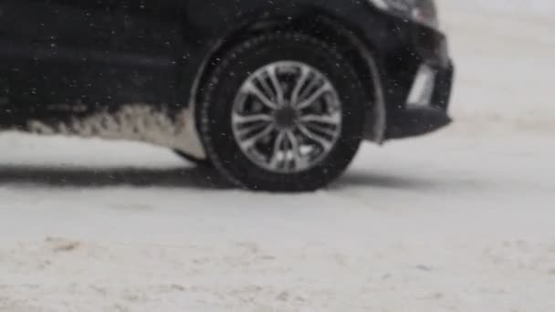 Samochód stoi na pokrytym śniegiem skrzyżowaniu w zimowym mieście. Śnieg. Zamknij koło w zwolnionym tempie. Ślady opon. Złe warunki pogodowe dla ruchu, śnieżyca. Niebezpieczeństwo podróży — Wideo stockowe