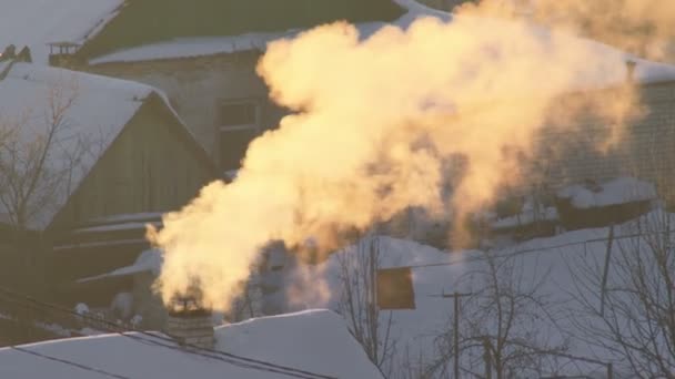 El humo de las chimeneas del pueblo sale al aire helado en invierno. Salida del sol naranja — Vídeo de stock
