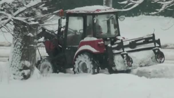Маленький трактор с мигающим светом и кистью едет по дороге, чтобы расчистить снег на тротуарах после снегопада. — стоковое видео