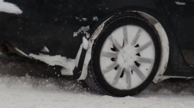 Araba kış şehrinde karla kaplı bir yolda gidiyor. Kar yağışı. Tekerleği yavaş çekimde kapat. Lastik izleri. Trafik ve kar fırtınası için kötü hava koşulları. Yolculuk tehlikesi