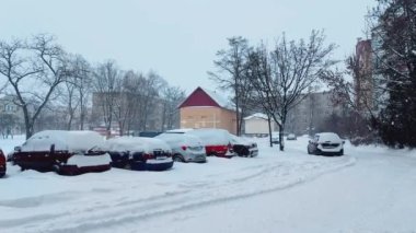 Kışın kar yağışı, kışın çok katlı bir binanın bahçesinde park halindeki arabaların arka planına vuruyor.