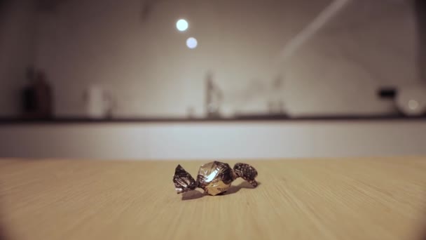 Chocolade snoep in een gouden wikkel ligt op de tafel thuis, close-up — Stockvideo