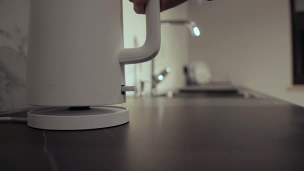 Мужчина ставит и включает белый электрический чайник на кухне — стоковое видео