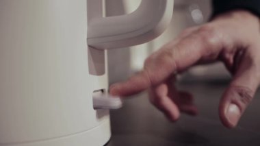 Adam mutfaktaki elektrikli çaydanlığı çalıştırıyor, yakın plan.