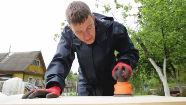 Un hombre pule la madera con una herramienta eléctrica, un primer plano. Madera hecha a mano, limpieza de madera con papel de lija — Vídeos de Stock