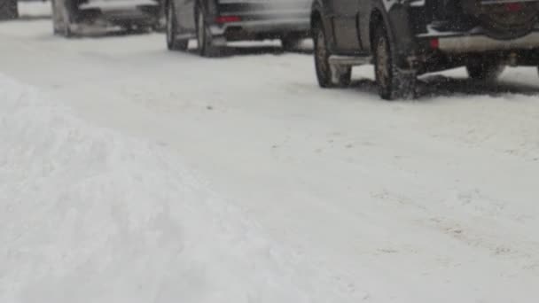 Auto 's rijden op een besneeuwde weg in de winterstad. Sneeuwval. Sluit het wiel in slow motion. Bandensporen. Slechte weersomstandigheden voor het verkeer, sneeuwstorm. Gevaar voor de reis — Stockvideo