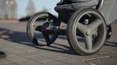 Bir kız temiz havada bebek arabasıyla yürüyor. Bir kızın bacakları kaldırım taşlarının üzerinde yürüyor, bebek arabasının tekerlekleri, yakın plan.