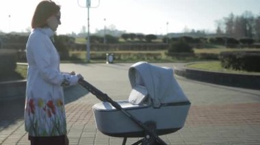 Gri paltolu ve siyah gözlüklü genç bir anne elinde bebek arabasıyla caddede yürüyor. Annelik ve aile, geçmiş, hareket
