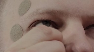 Yüz ve gözler için bitkisel alan, görüşü geliştirmek için, yüz kaslarını gevşetmek için. Yüzünde yuvarlak bir bitkisel yama olan bir adam. Yakın plan.