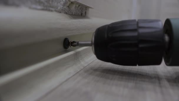 Pekerja mengencangkan sekrup dengan obeng ketika menginstal papan rok. Renovasi apartemen, close-up — Stok Video