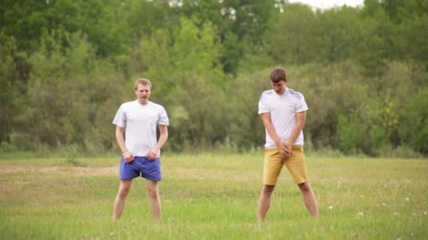 Dva mladí kluci chodí na sport v přírodě dělat sestupné ohyby a protahování, zázemí. Cvičení — Stock video