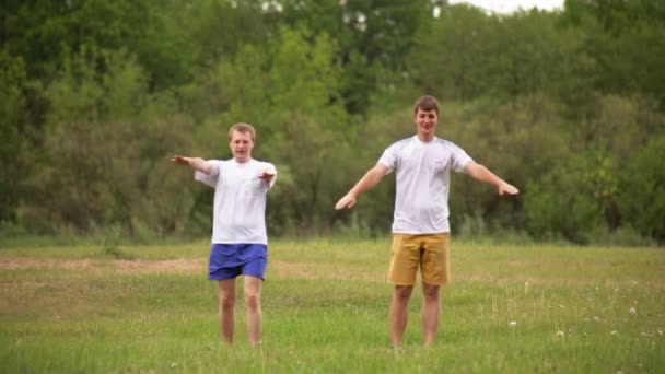 Két jóképű fiatal srác megy be sportolni és sportolni a természetben, a zöld fák hátterében. Szabadtéri sport koncepció, egészséges életmód, edzés — Stock videók