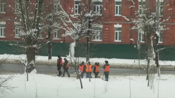 Un escuadrón de conserjes en chalecos naranjas están limpiando la nieve en la ciudad — Vídeo de stock