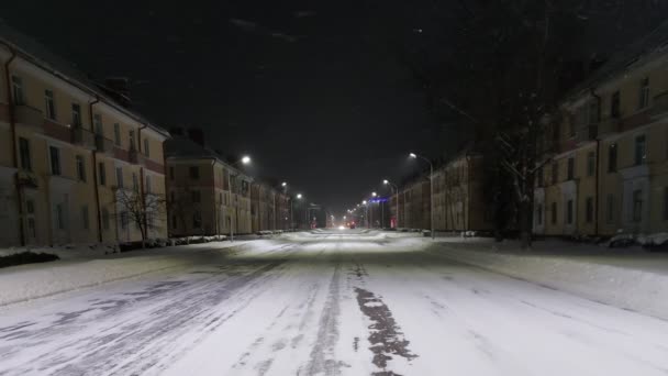 Geceleri bir kış şehrinde boş bir yol. Trafik ışığı turuncu yanıp sönüyor. Şehir ışıklandırması. Hava şartları. Yol boyunca üç katlı eski binalar — Stok video