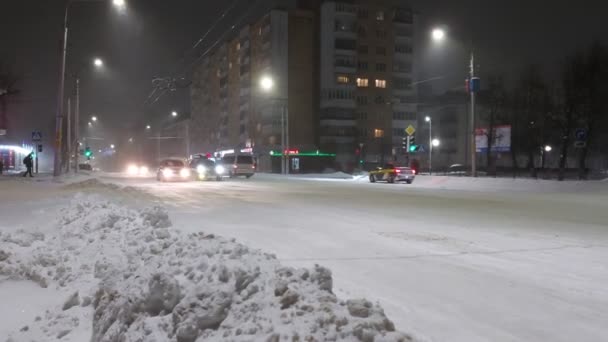 車は街の冬の夜の通りに沿って運転します。道路は雪で覆われている。交通事故の滑りや発生の危険性。悪天候。都市照明 — ストック動画